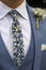 Vertical shot of a groom wearing a blue three-piece suit with a stylish tie with a floral print