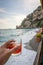 Vertical shot of a hand holding a drink on Positano Amalfi coast background