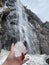 Vertical shot of a hand holding ice with Pissevache waterfall in the background in Switzerland