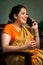 Vertical shot of happy indian woman talking on mobile phone while sitting on chair at home - concept of relaxation