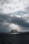 Vertical shot of an iceberg in an open sea with sunlight on and gloomy sky in the background