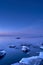 Vertical shot of an idyllic frozen rocky shore with blue and pink sunset in the background