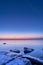 Vertical shot of an idyllic frozen rocky shore with blue and pink sunset in the background