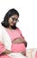 a vertical shot of an indian pregnant lady wearing spectacles in pink dress caressing her baby bump belly in white