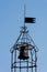 Vertical shot of an iron forged weather vane and bell with a blue clear sky behind