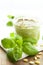 Vertical shot of a jar of pesto next to basil leaves and pine nuts