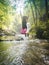 Vertical shot of a joyful female jumping in a river with a waterfall in the background