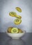 Vertical shot of kiwi slices falling into a white plate