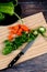 Vertical shot of a knife, chopped carrots peppers on a wooden board, and green peppers on a plate