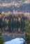 Vertical shot of a lake with the reflection of the tall and colorful trees visible on the calm water