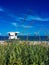 Vertical shot of a lifeguard tower and sandy beach ocean behind a green grass bush on a cloudy day