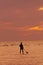 Vertical shot of a man silhouette surfing in the empty sea under an orange and pink sky at sunset