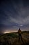 Vertical shot of a man standing on the rocks and looking at the shining stars in the night