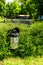 Vertical shot of a metal recycling bin in the middle of green bushes in a park next to a street