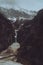 Vertical shot of a narrow waterfall cascading from snowy mountains over rugged cliffs