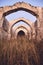 Vertical shot of an old ancient ruin with an arched ceiling in a dry grassy field under a blue sky