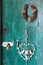 Vertical shot of an old green wooden door with a padlock, wreath and white metal candle holder