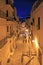 Vertical shot of a pathway in the middle of buildings with lit street lights at night time