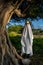 Vertical shot of a person covered by a white sheet, with sunglasses and hat,in appearance of a ghost