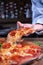 Vertical shot of a person getting a piece of delicious cheesy pepperoni pizza