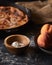 Vertical shot of a pie and a bowl of peaches on a black surface covered with flour