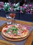 Vertical shot of a pizza with ham and tomatoes on a wooden board on the table with drinks on it