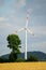 Vertical shot of a renewable energy windmill, green trees and a background of sky with clouds