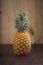 Vertical shot of a Ripe Tropical Pinapple on a wooden table with a wooden background.