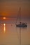 Vertical shot of a sailboat traveling across the sea with a beautiful sunrise and an orange sky