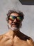 Vertical shot of a shirtless middle-aged man with colorful perforated glasses under the sun