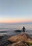 Vertical shot of a single person standing on a massive rock in a sea