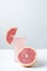 Vertical shot.Slice of grapefruit on the glass of juice and cutted grapefruit on the wite surface against grey background