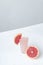 Vertical shot.Slice of grapefruit on the glass of juice and cutted grapefruit on the wite surface against grey background