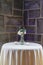 Vertical shot of a small vase with white roses on a small white table in front of a stone wall