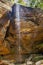 Vertical shot of a small waterfall flowing down from a rocky cliff in a tropical cave