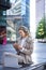 Vertical shot of smiling adult woman studying outdoors, listening to online course, taking notes, attend team meeting