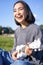 Vertical shot of smiling asian girl singing and laughing, playing ukulele, learn how to play instrument, sitting