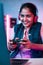 Vertical shot, Smiling girl playing live video game on laptop by talking on headphones at home on neon background -