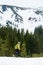 Vertical shot of snow-covered mountain and off-piste skier. Side view of male walking alone on ski at foot of mountain