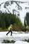 Vertical shot of snow-covered mountain and off-piste skier. Side view of male walking alone on ski at foot of mountain