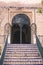 Vertical shot of a staircase leading to a building entrance with wrought iron gate and woody vines