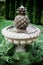 Vertical shot of a stone birdbath with a pineapple-shaped fountain in a beautiful green garden