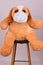 Vertical shot of a stuffed fluffy bear with a protective medical face mask on a chair