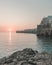 Vertical shot of the sunset reflecting on the sea and some buildings on a cliff