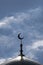 Vertical shot. The symbol of Islam is a golden crescent moon on top of the mosque minaret on the blue sky with clouds.