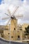 Vertical shot of the Ta Kola Windmill in the island of Gozo, Malta with buildings in the background.