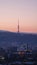 Vertical shot of a tall radio tower standing on a hill under a red sky at sunset in a city