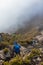 Vertical shot of two hikers descending the rocky mountain with clouds of mist on top of Cerro Chirripo in Chirripo National Park