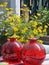 Vertical shot of two large red round vases in front of colorful blooming flowers
