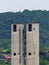 Vertical shot of two tall factory chimneys with a background of a forested mountain